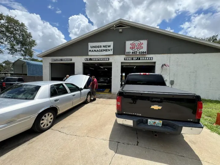 Auto repair shop exterior with two parked vehicles and people near the open garage bays