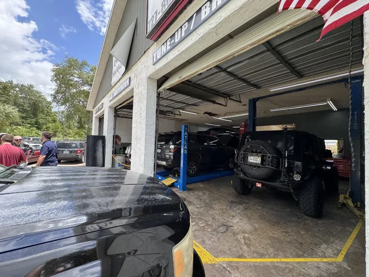 Auto repair shop with lifted off-road vehicles inside and an American flag above the bay