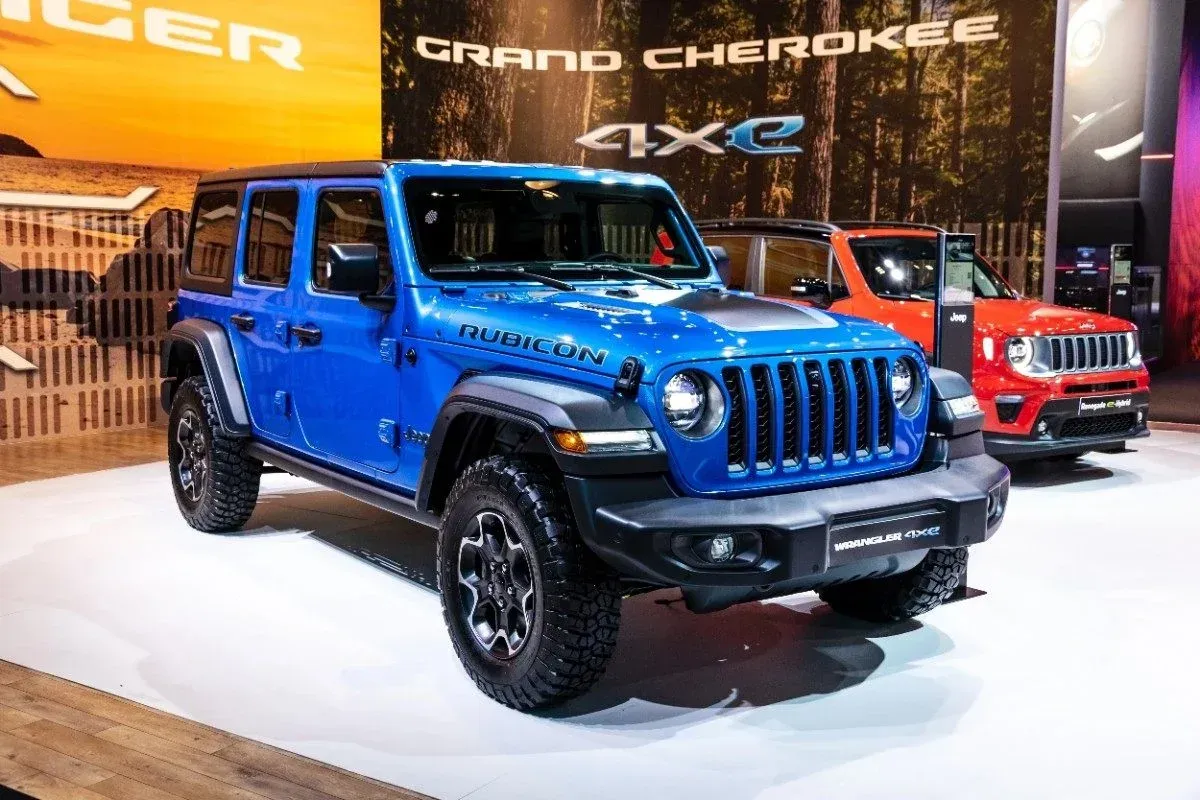 Blue Jeep Wrangler on display at an auto show, with a red Jeep in the background