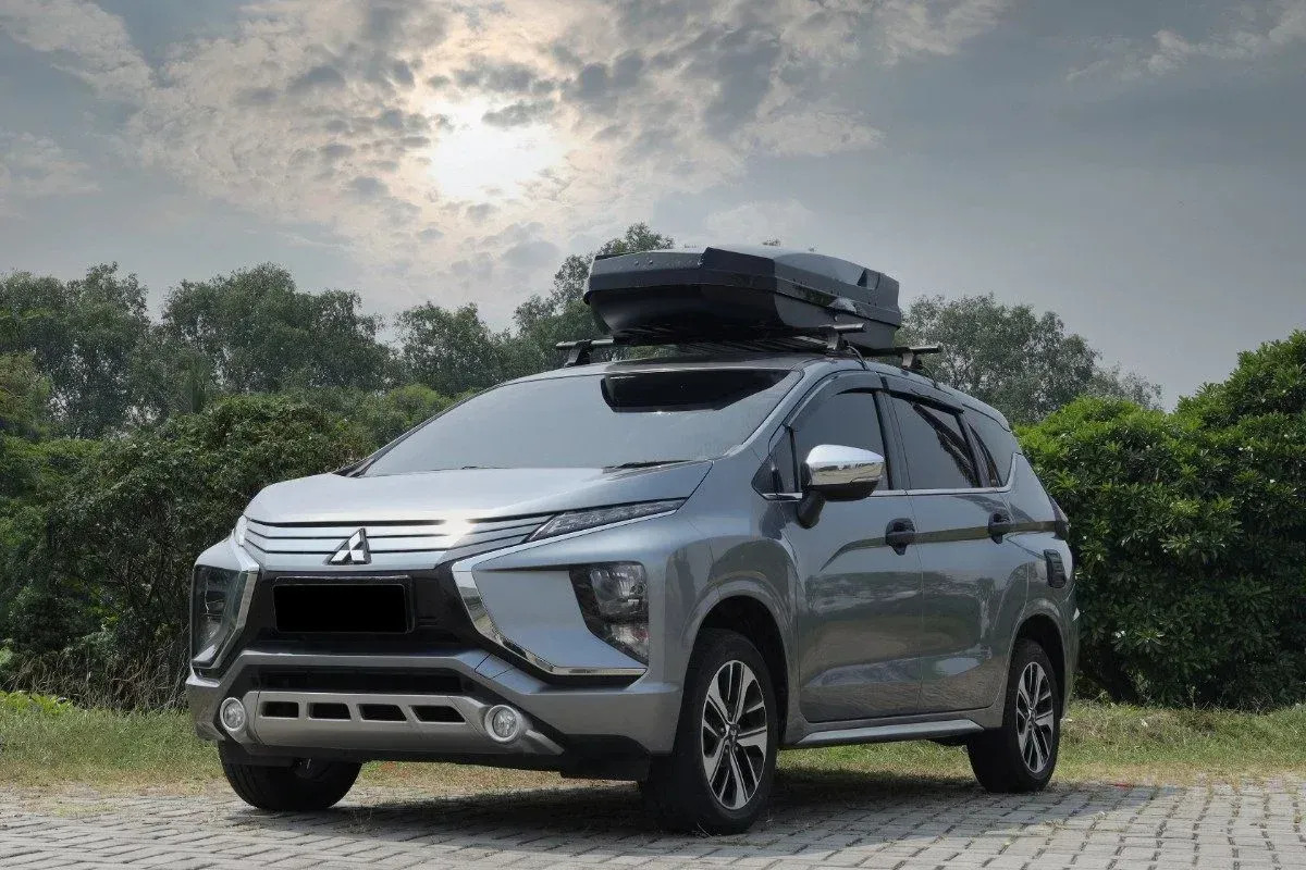 Silver SUV parked outdoors on a paved road, with a roof cargo box and cloudy sky behind.