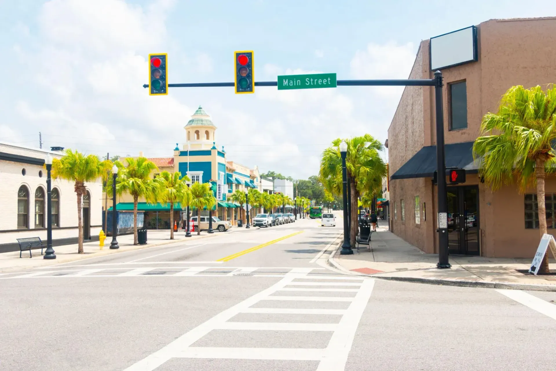 Empty city street with traffic lights, crosswalk, palm trees, and a domed building in the distance