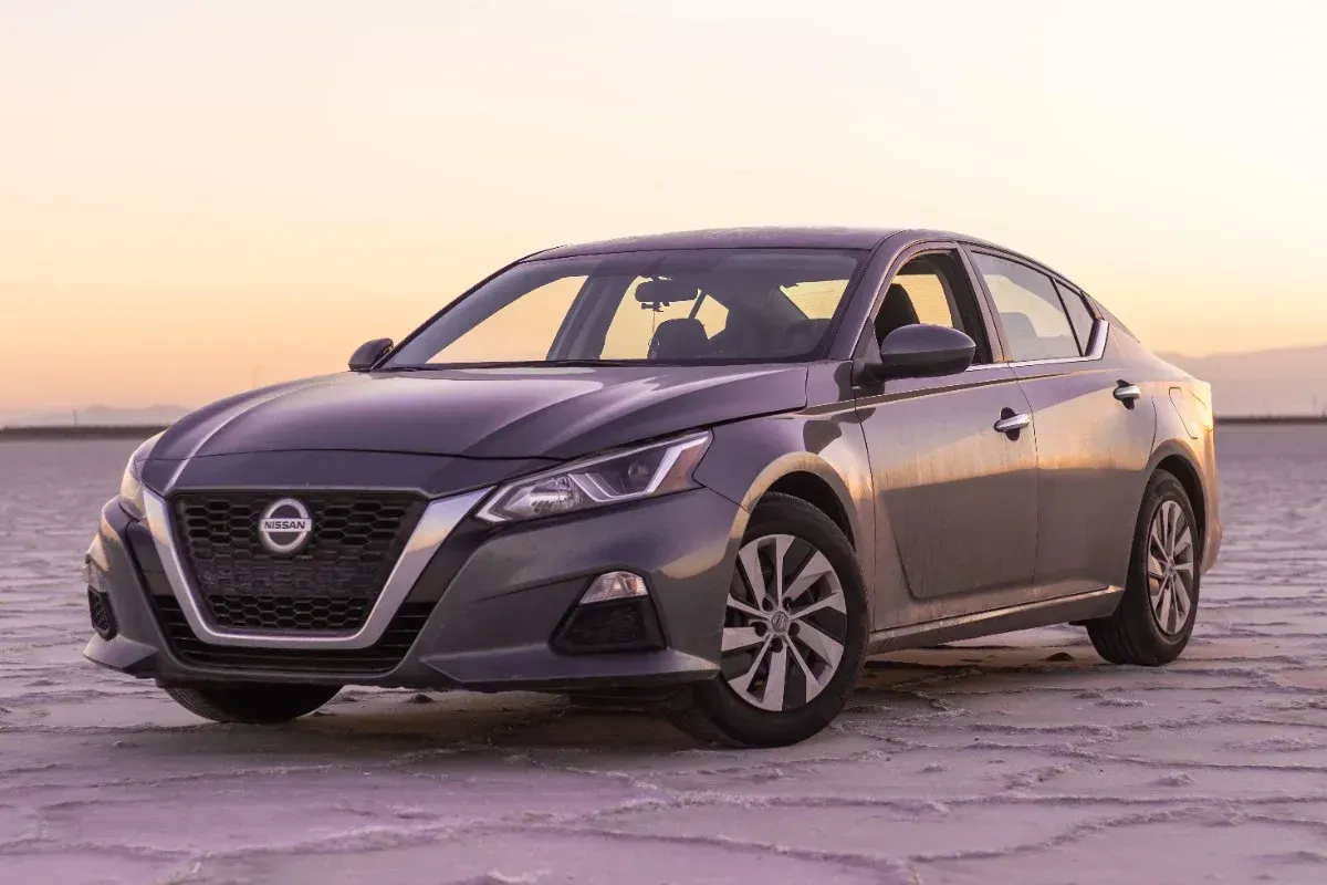 Gray Nissan sedan parked on a beach at sunset.