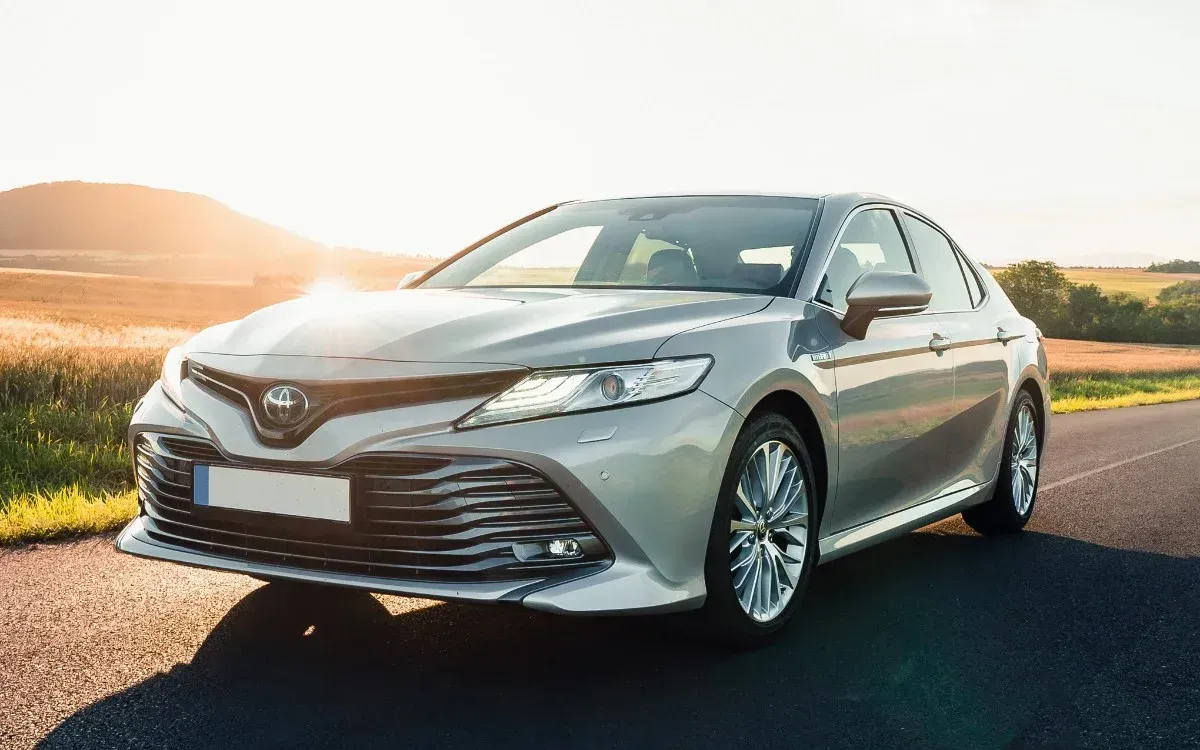 Silver sedan driving on a sunny road at sunset, front view with mountains in the background