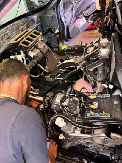 Mechanic working inside a car’s stripped interior with dashboard removed and exposed wiring