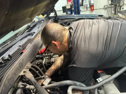 Mechanic working under a car hood in a garage, inspecting the engine