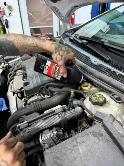 Mechanic pouring red automotive fluid into a car engine bay near the windshield.