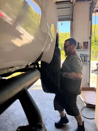 Mechanic inspecting a lifted white truck in a garage, wearing dark work clothes.