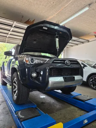 Black Toyota SUV on a blue alignment lift with hood open in a garage