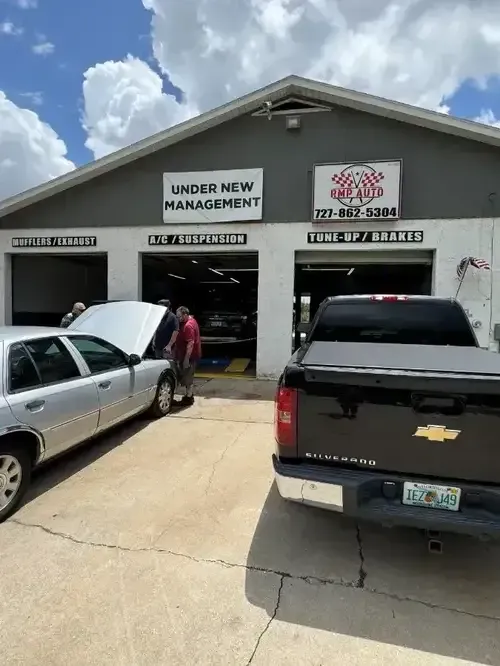 Auto repair shop exterior with parked silver sedan, white SUV, and black pickup truck under a cloudy sky