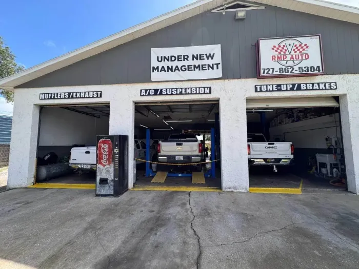 Auto repair shop with three service bays and cars inside, under new management sign overhead