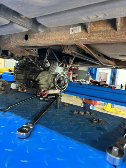 Car on a blue lift in an auto shop, with a transmission or engine assembly exposed underneath.