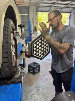 Mechanic holding a wheel alignment tool beside a lifted vehicle in an auto shop