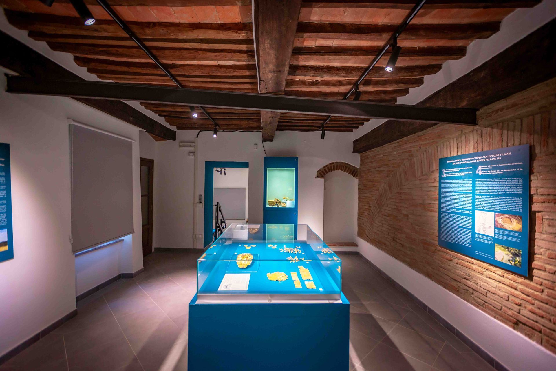 Exhibition room with central case and bilingual panels on the brick wall