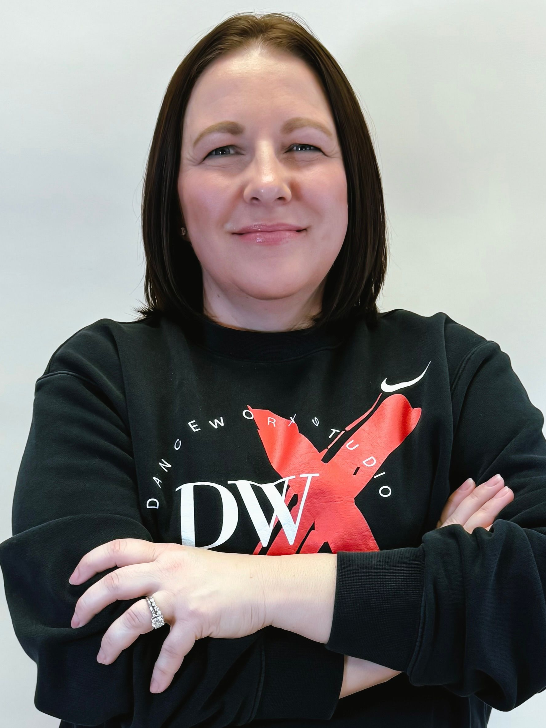 Woman standing with arms crossed, wearing a black sweatshirt with a red X and white “DW” logo.