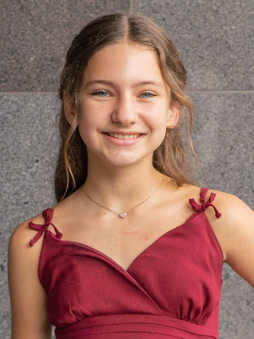 Smiling person in a burgundy dress against a gray stone wall.