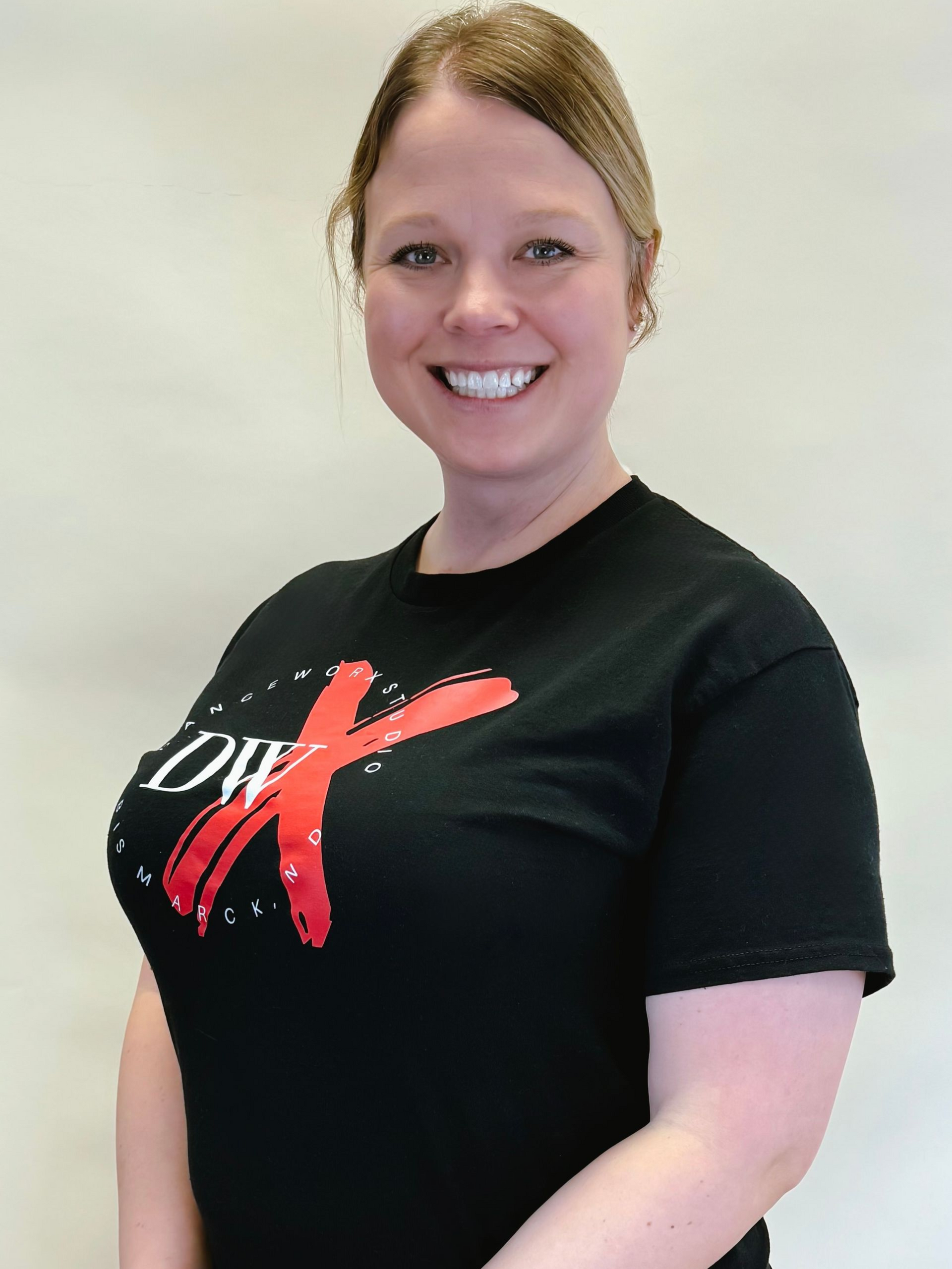 Smiling person in a black T-shirt with a red-and-white logo, standing against a plain light background