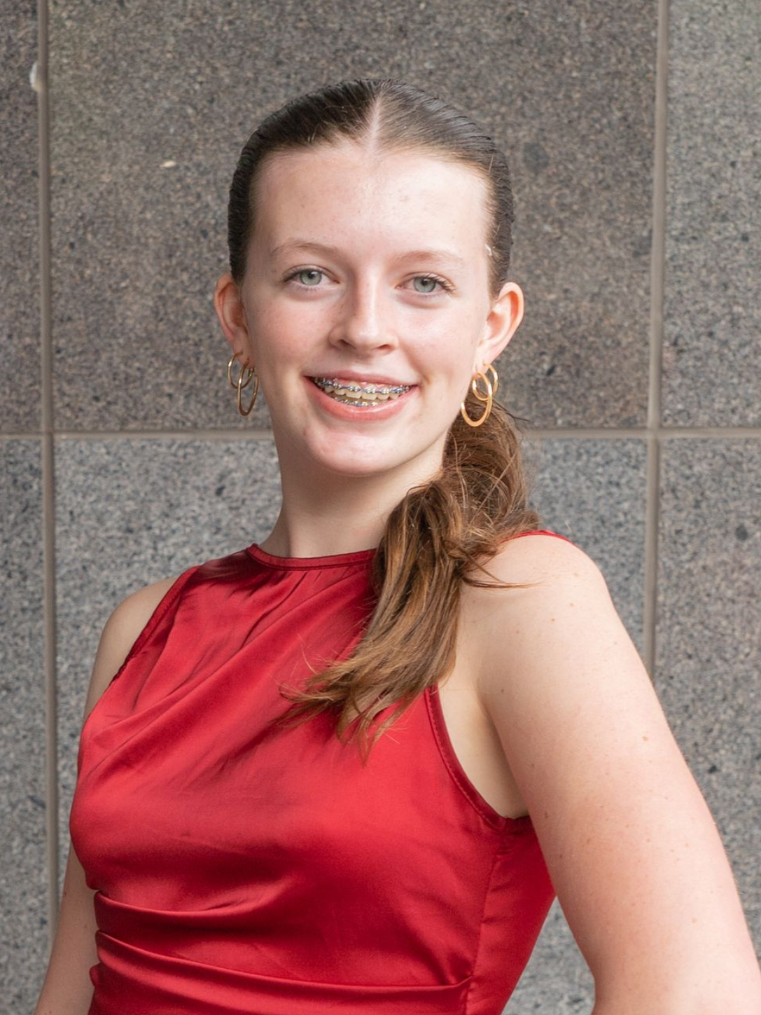 Person in a red sleeveless top smiling against a gray tiled wall.