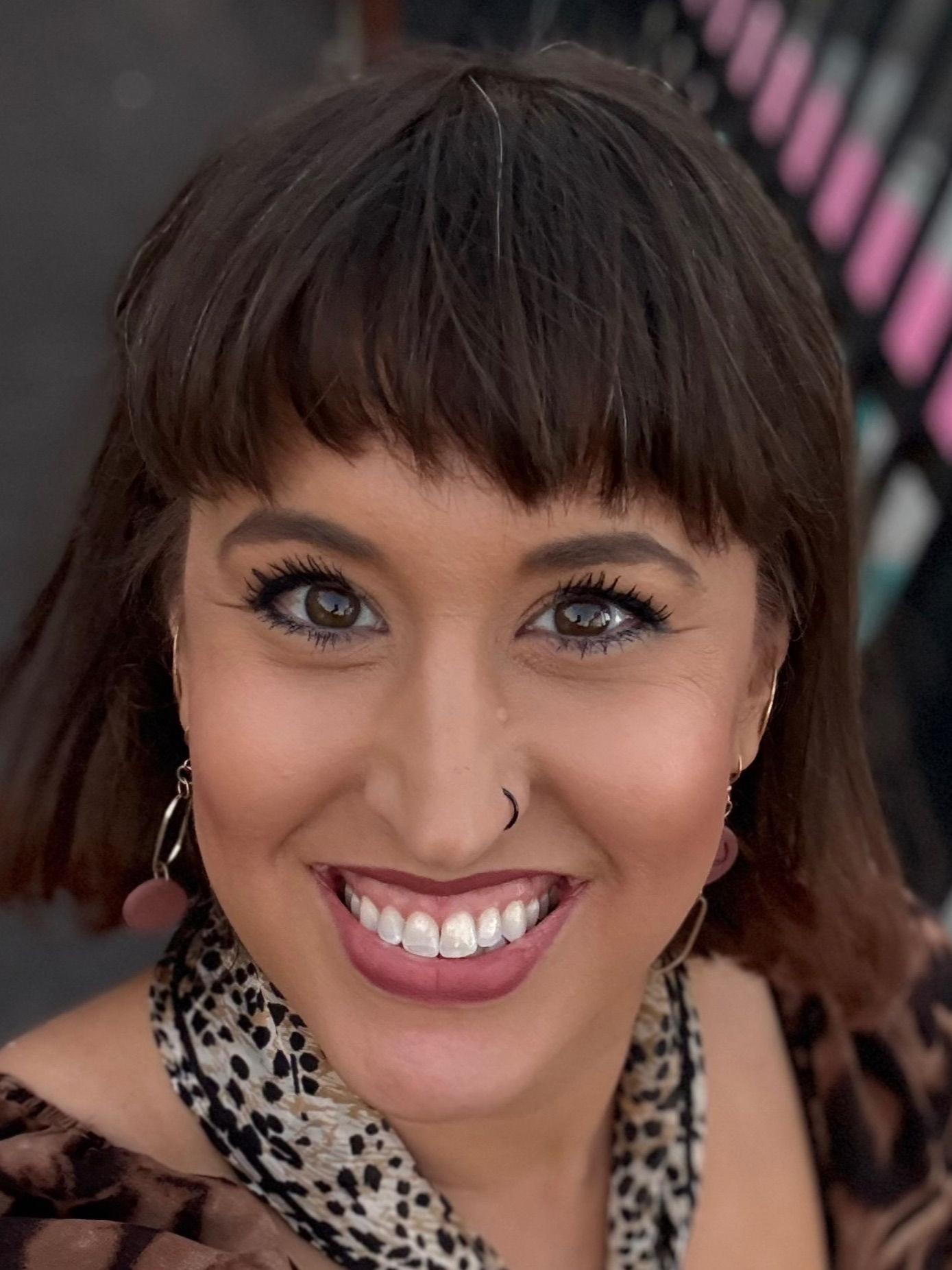 Smiling woman with short dark hair and a leopard-print top, wearing earrings, against a blurred background