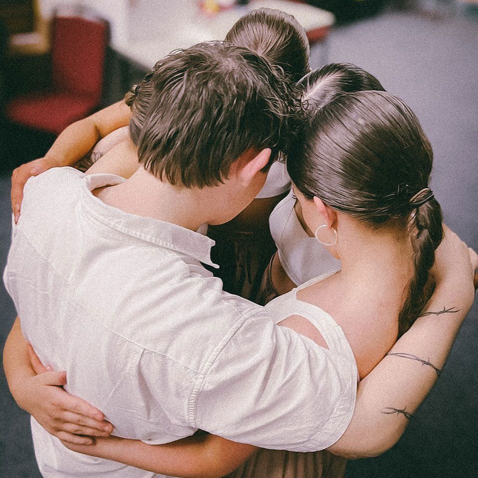 Two people embracing closely indoors, viewed from behind in a warm, dim setting