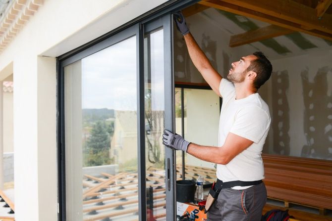 Worker installing a sliding glass door in a home interior, reaching up with tools