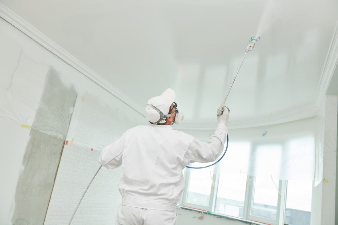 Person painting a white ceiling and walls in a bright room, using a roller on a long handle