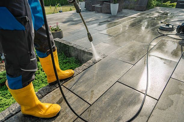 Person pressure-washing a stone patio with yellow boots and black pants