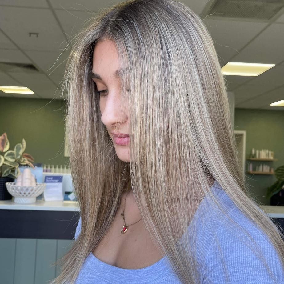 Woman With Long Straight Blonde Hair In A Blue Top, Standing Indoors Near A Counter — Blackwell Hair In Woree, QLD