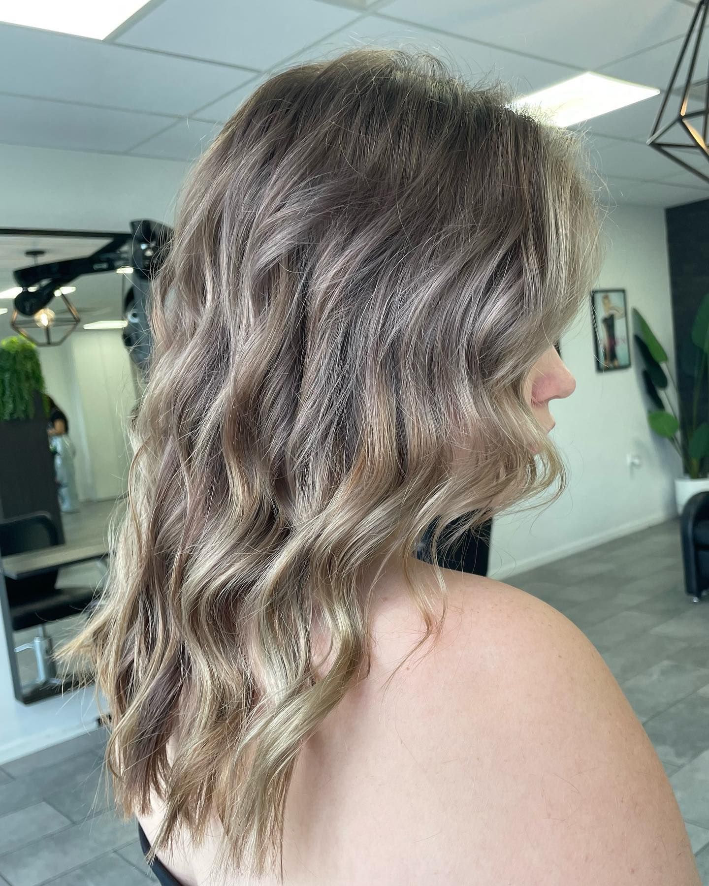A woman with long wavy hair is standing in a salon — Blackwell Hair In Woree, QLD