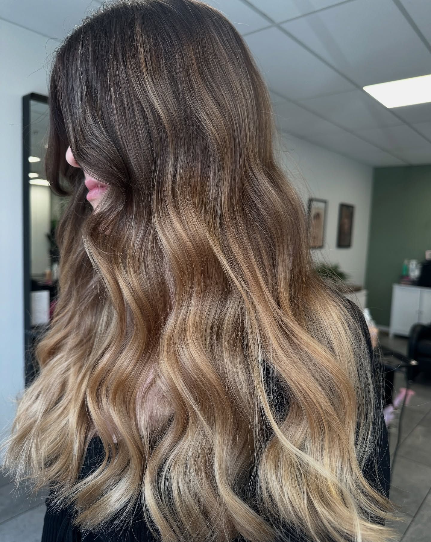 Long wavy brown hair with blonde ombré highlights in a salon setting