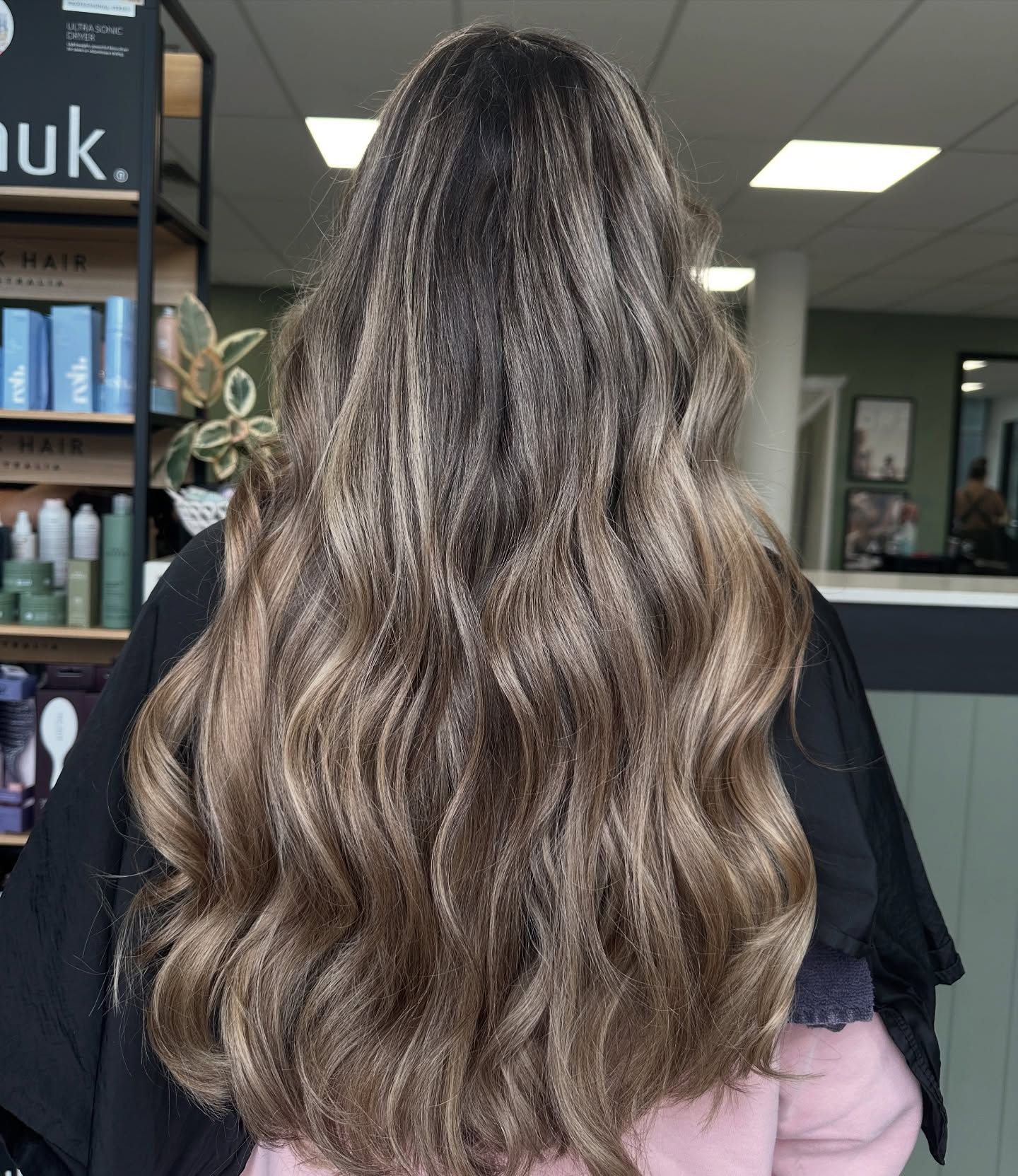 Back view of long wavy brown hair with blonde highlights in a salon interior
