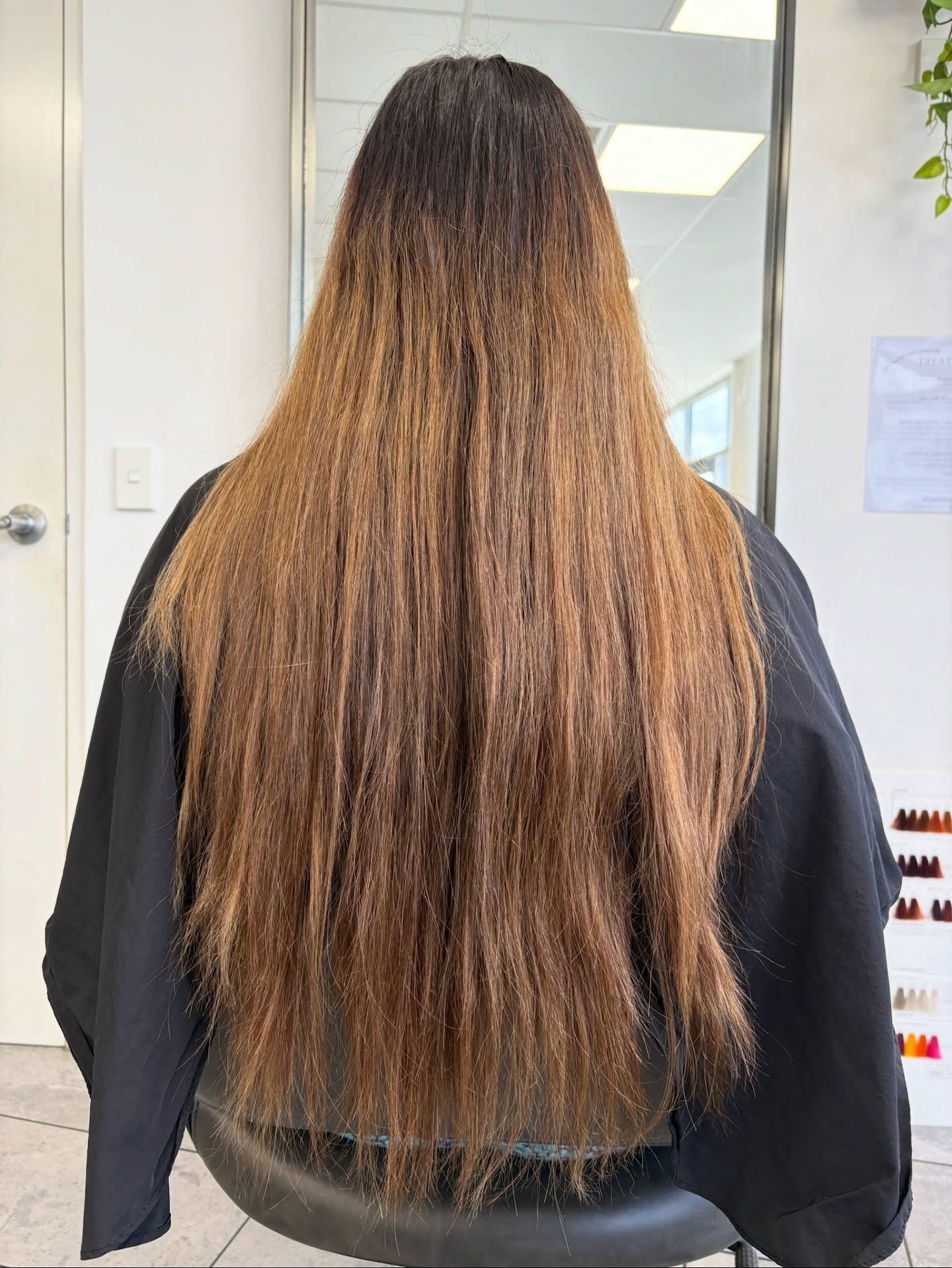 Person with long brown hair seen from behind in a salon chair, wearing a black cape