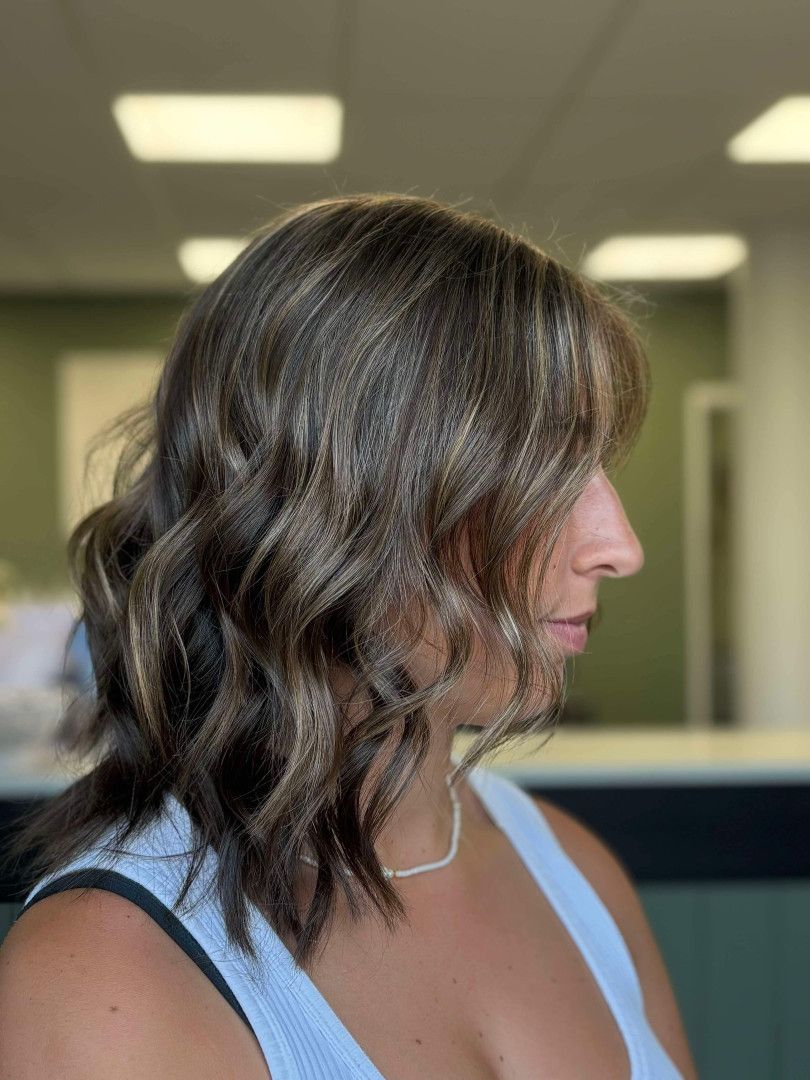 Side Profile Of A Woman With Wavy Dark Hair In A Light Blue Top Indoors — Blackwell Hair In Woree, QLD