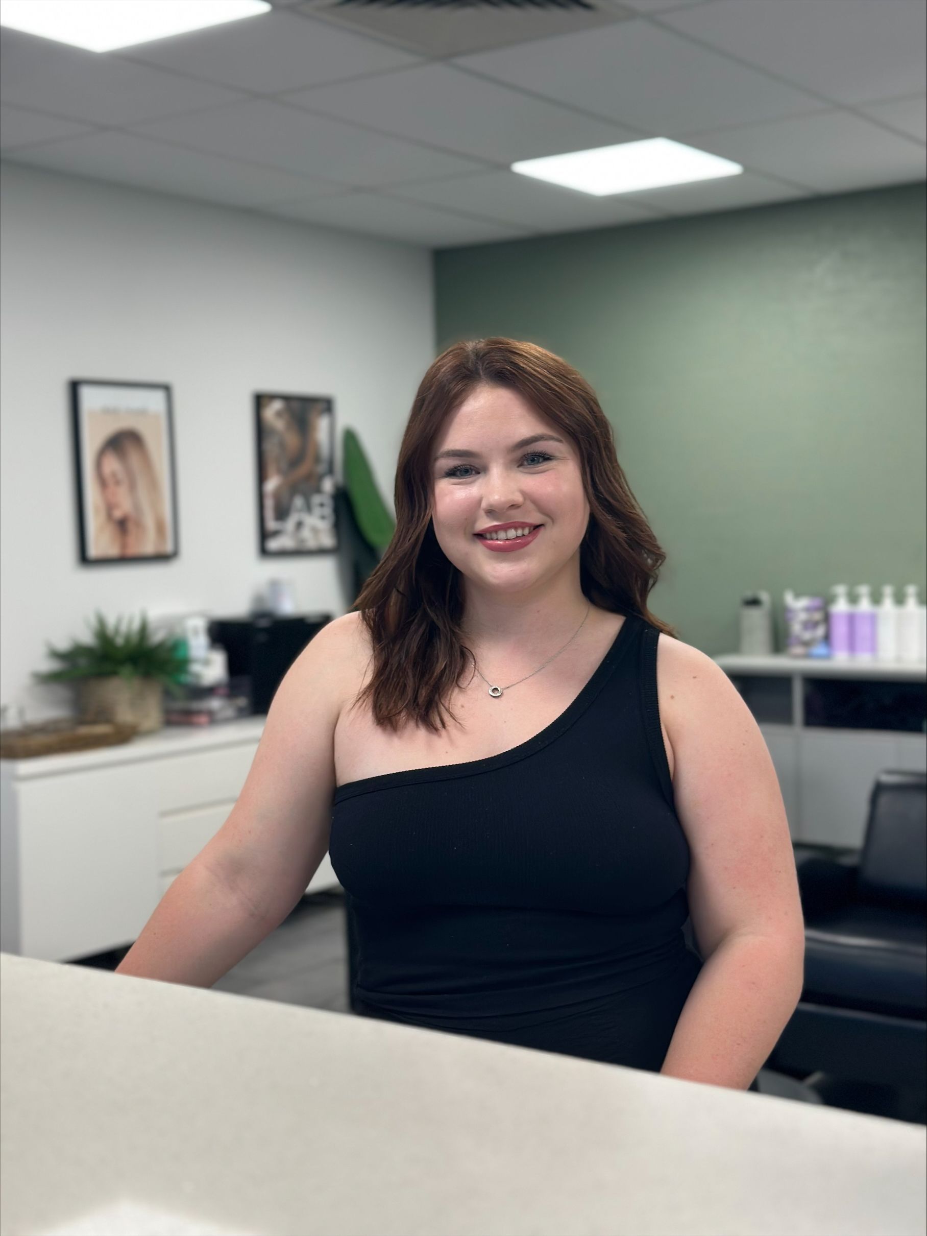 A woman in a black tank top is sitting at a counter in a salon — Blackwell Hair In Woree, QLD