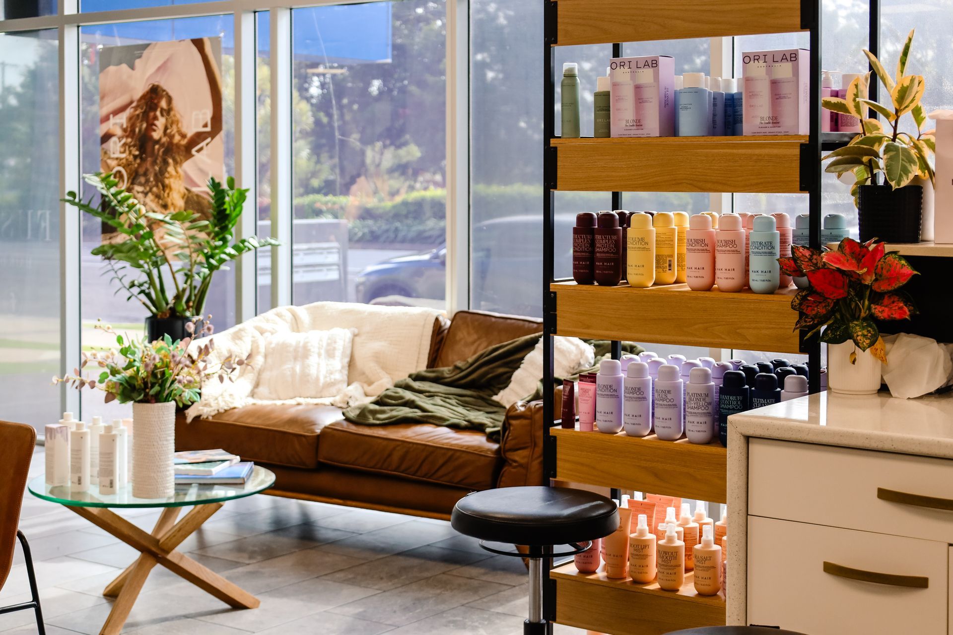 Bright, modern room with a sofa, glass table, and product shelf by large windows