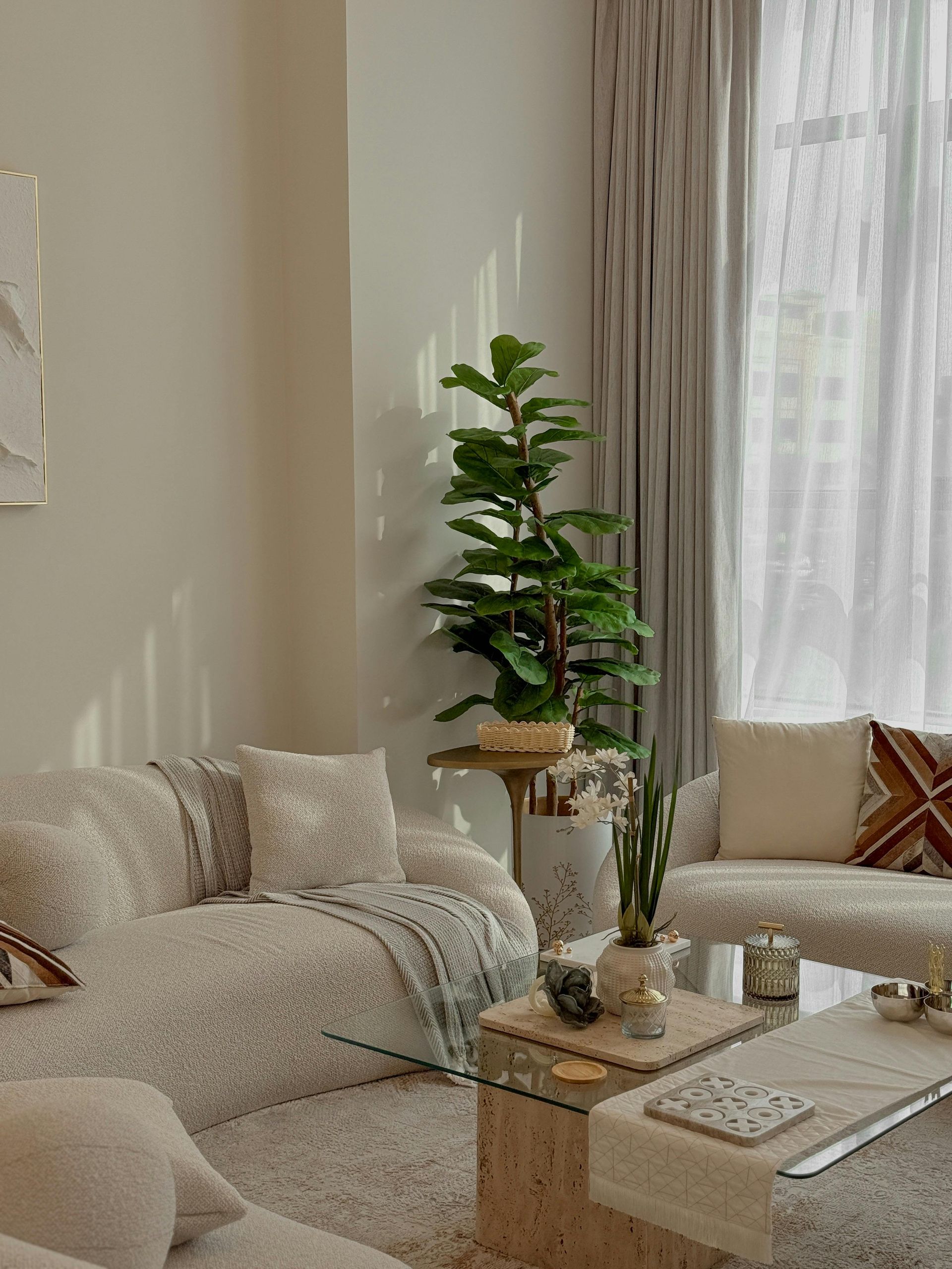 Cozy beige living room with a sectional sofa, coffee table, plants, and sheer curtains by a bright window