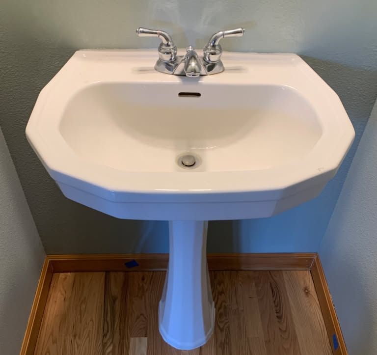 White pedestal sink with chrome faucet in a small bathroom with green walls and wood floor.