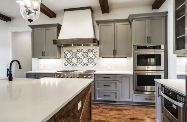 Modern gray-and-white kitchen with island, patterned backsplash, wood floors, and double wall oven