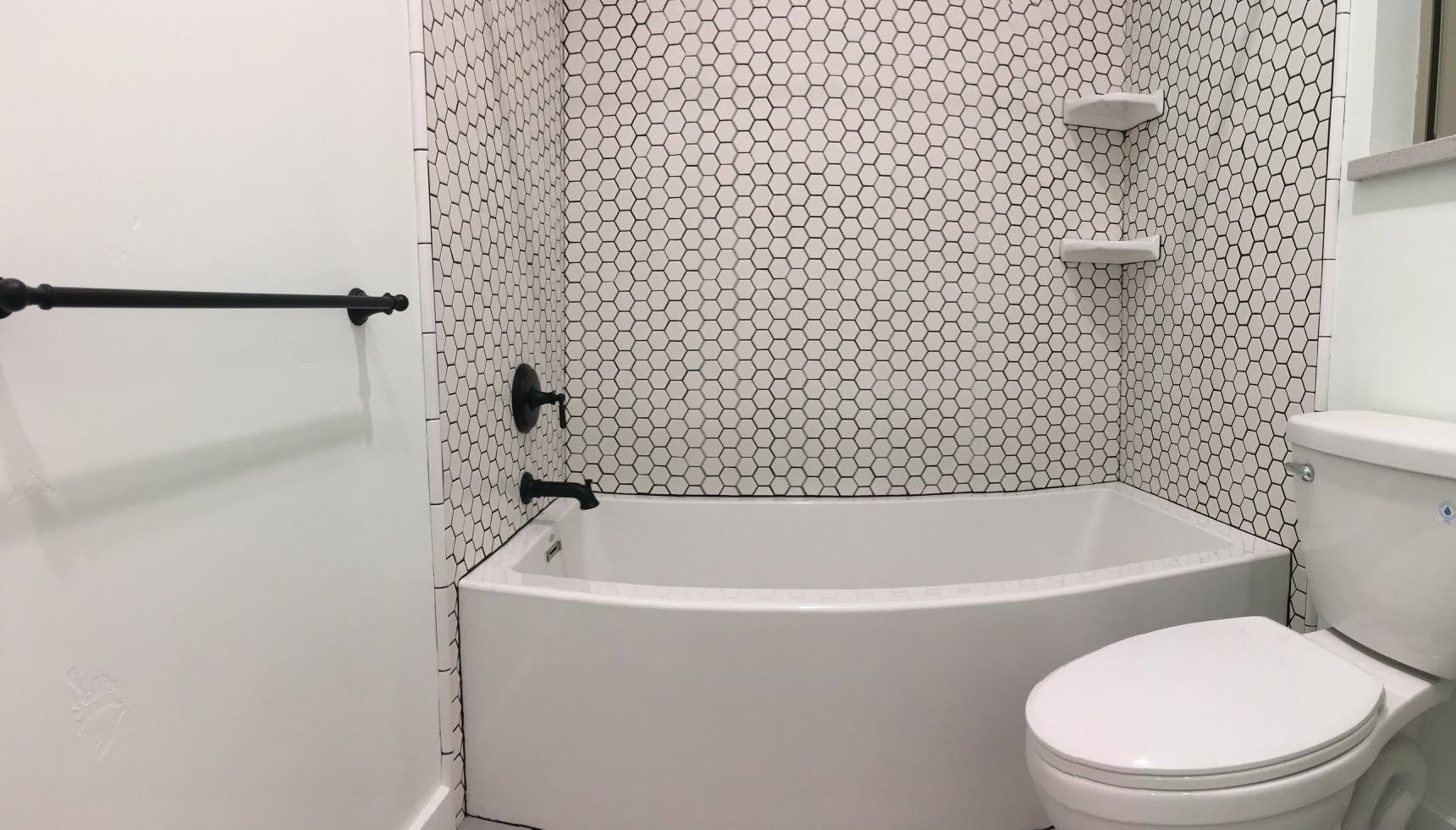 Small white bathroom with a shower-tub, hex tile wall, and toilet.