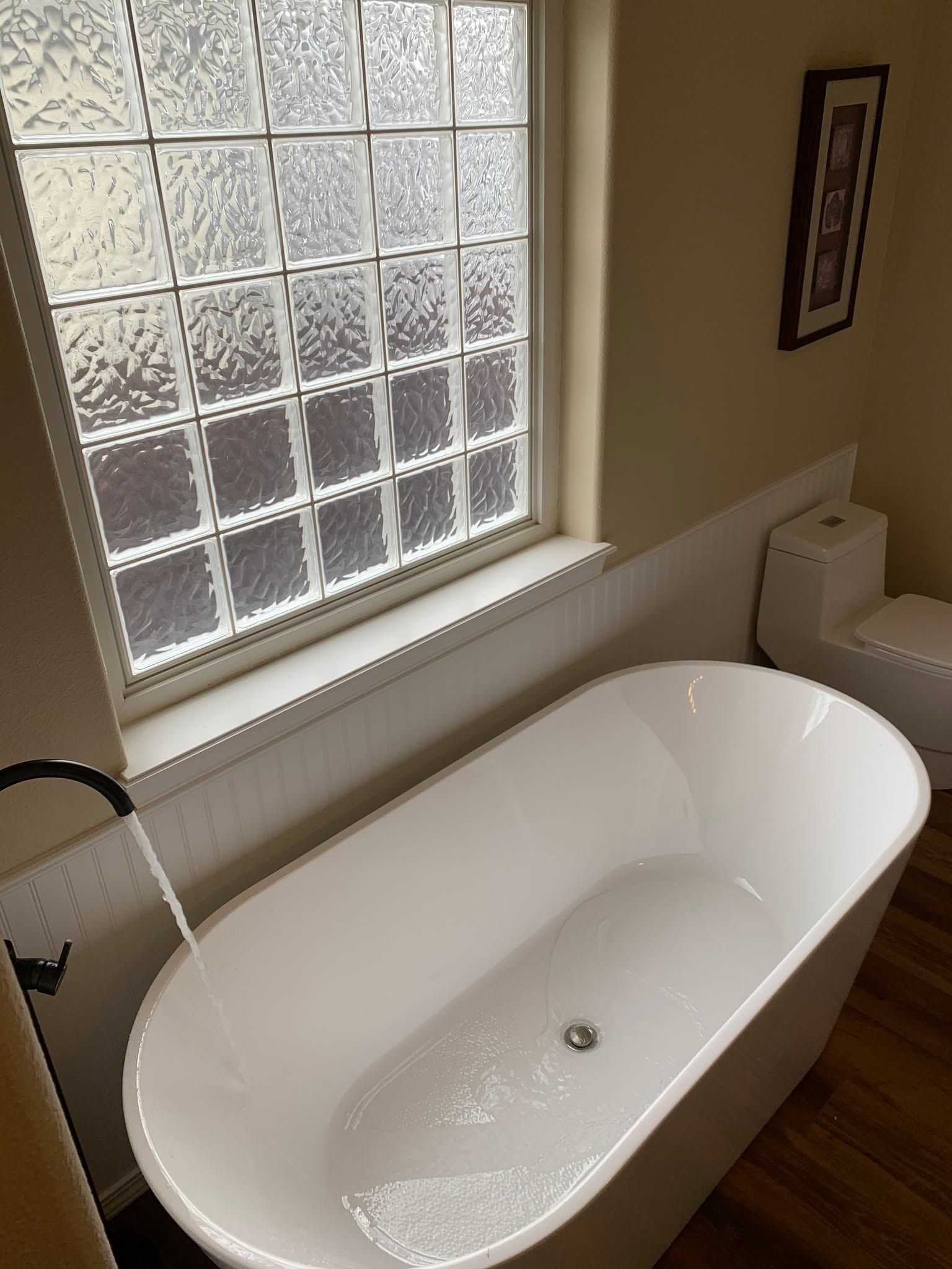 White freestanding bathtub beside a frosted window in a bright bathroom