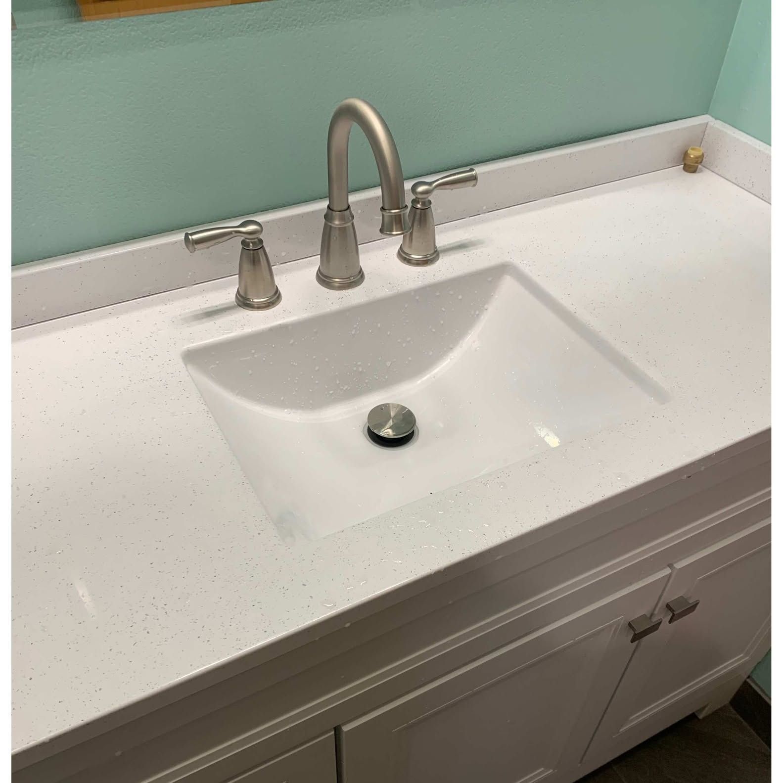 Bathroom vanity with white sink, chrome faucet, and speckled countertop against a pale green wall