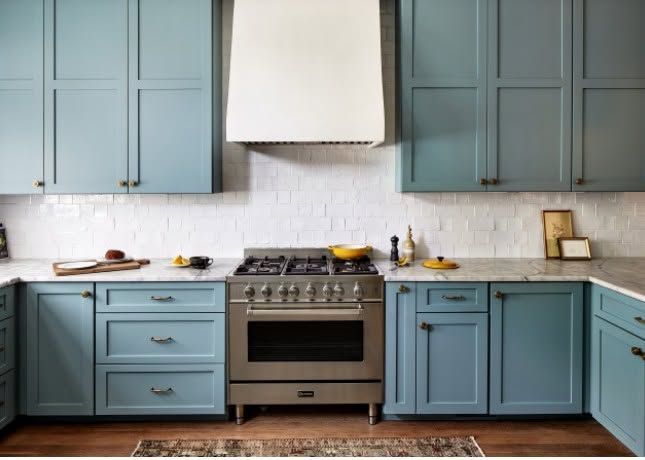 Blue kitchen with white range hood, stove, and light countertops against paneled cabinets