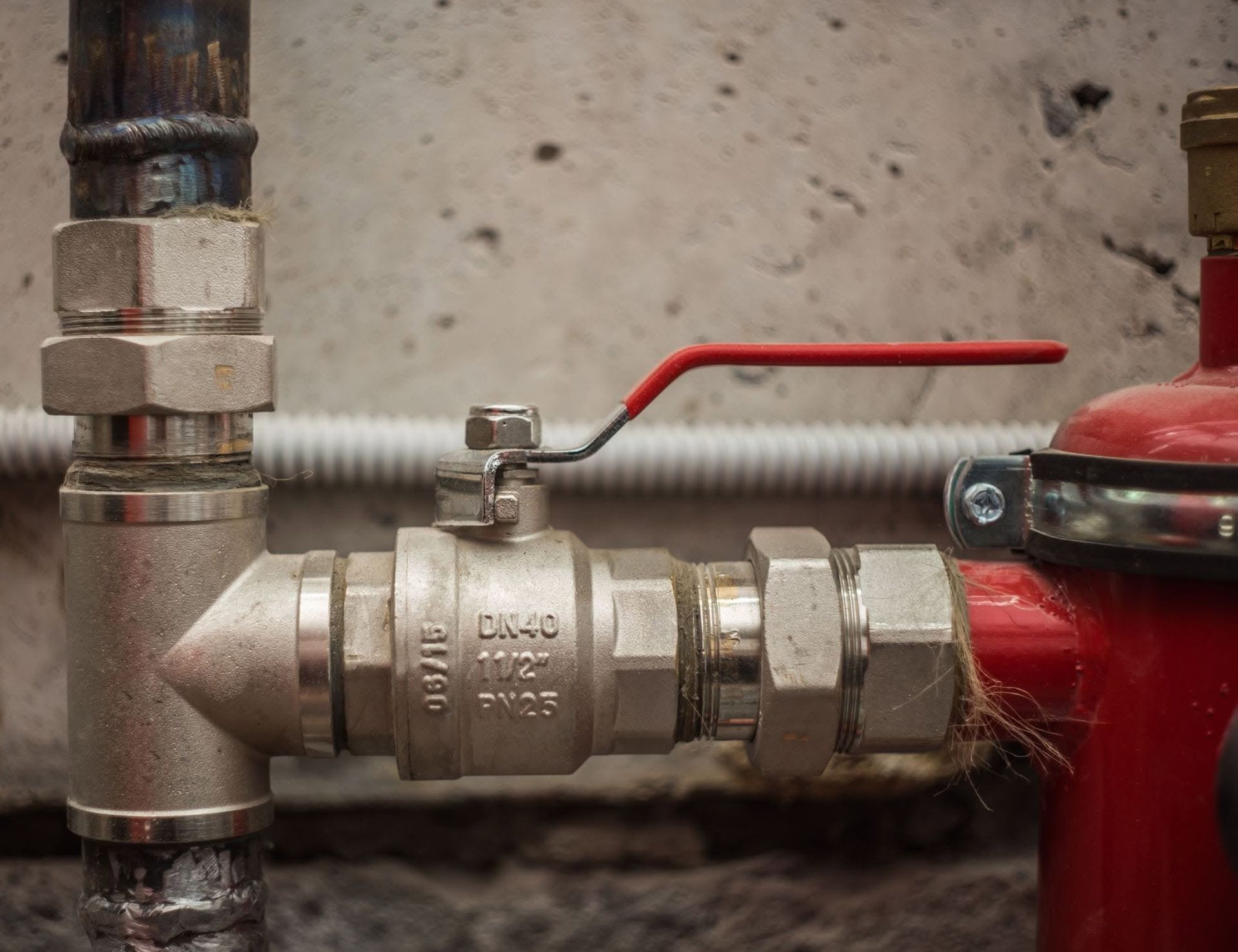 Close-up of a metal pipe valve with a red lever connected to a red tank or pump.