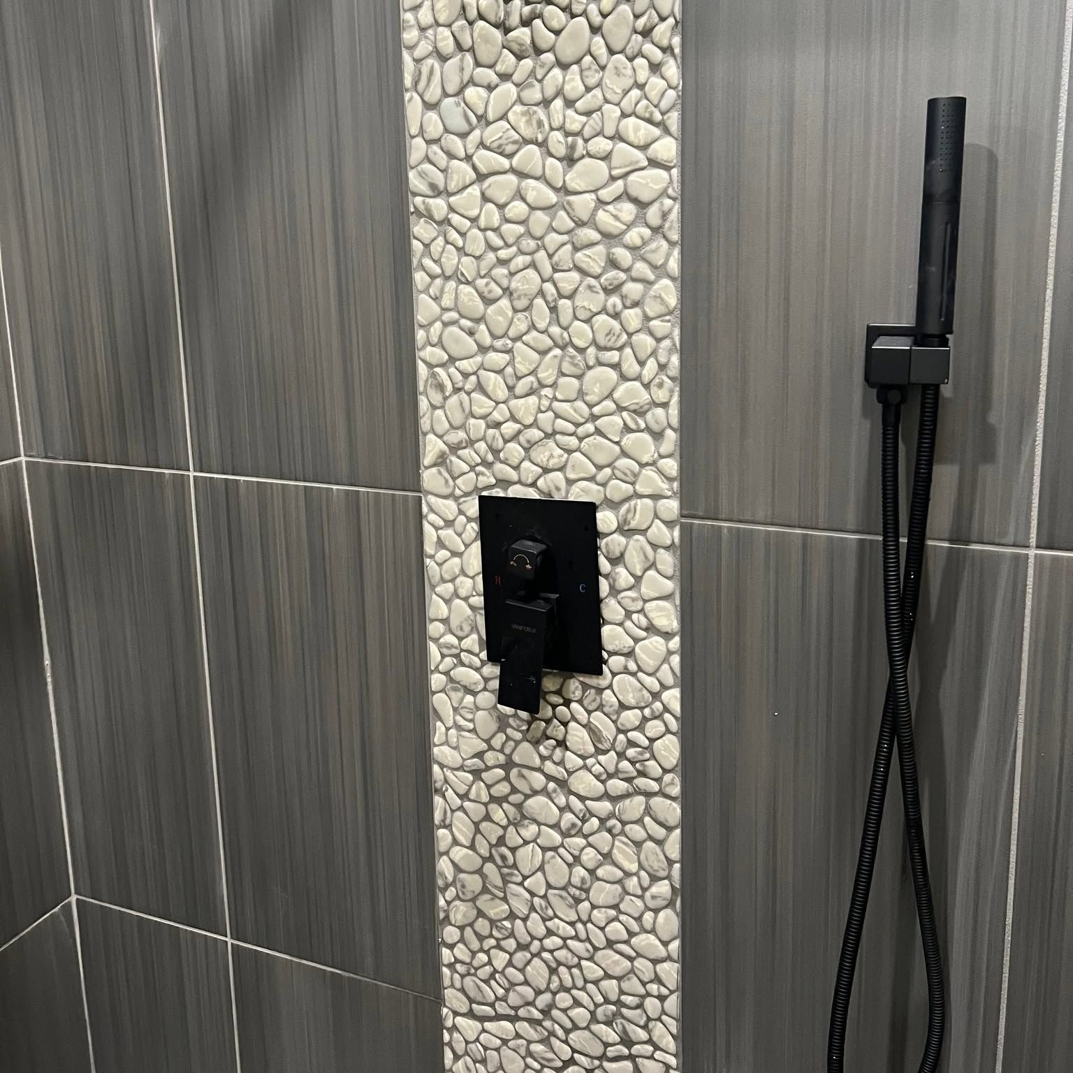 Shower wall with gray tile, pebble accent strip, recessed niche, and handheld shower sprayer