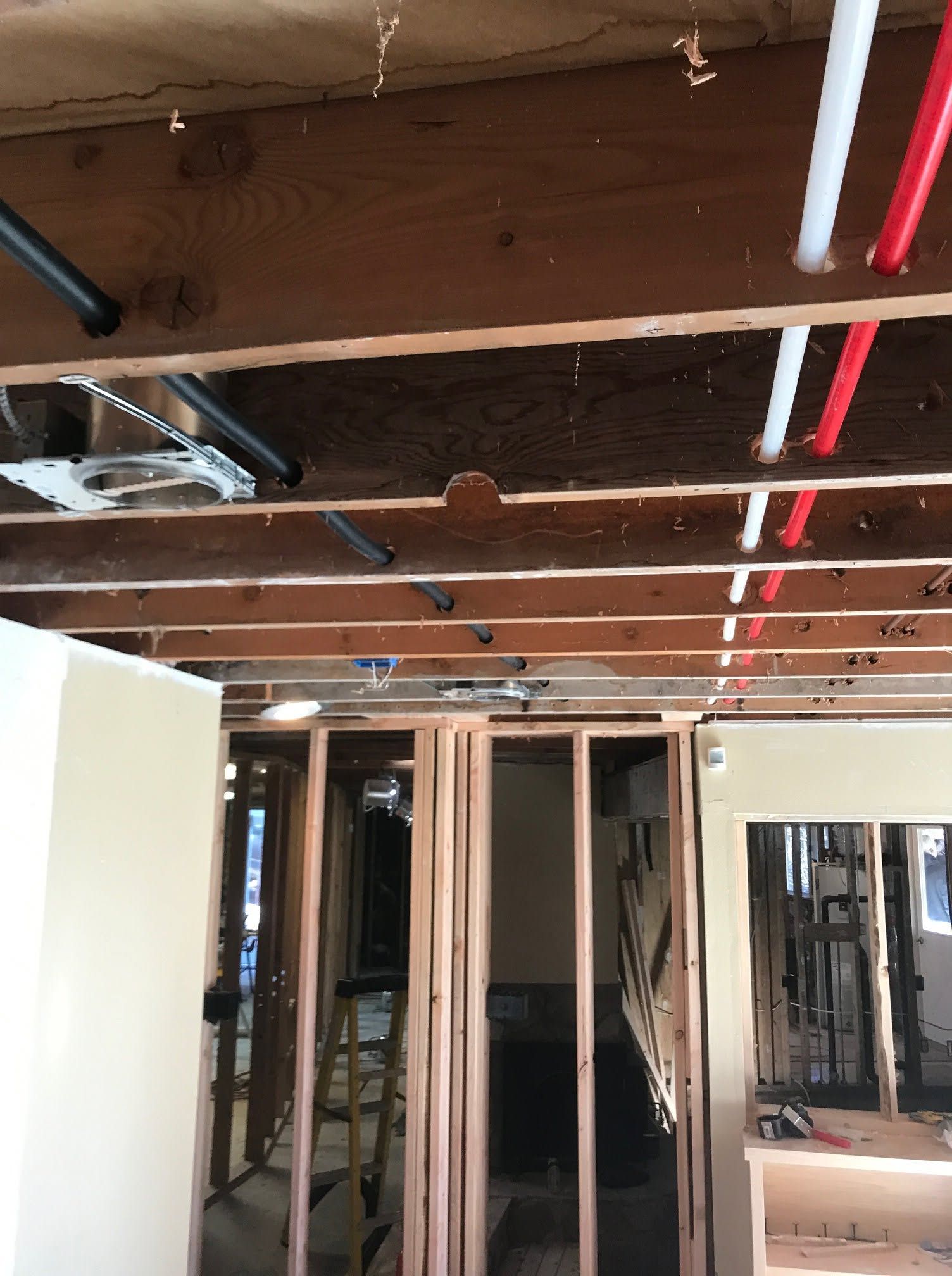 Exposed ceiling joists and plumbing in a gutted room under renovation.
