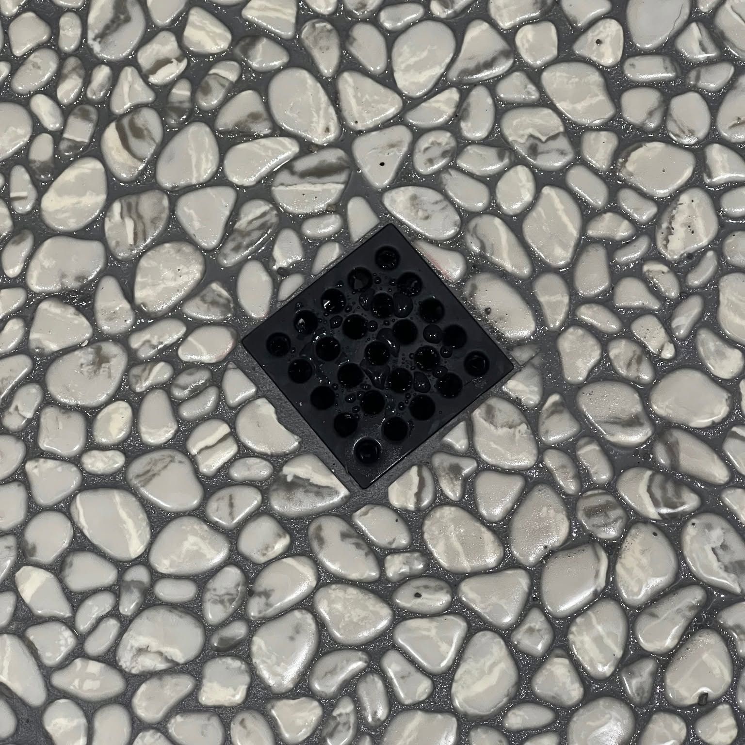 Black square drain cover on gray pebble-pattern pavement.