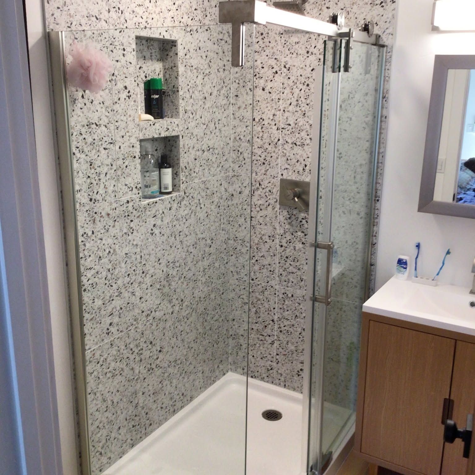 Modern bathroom shower with glass door, speckled tile walls, built-in shelves, and white shower base