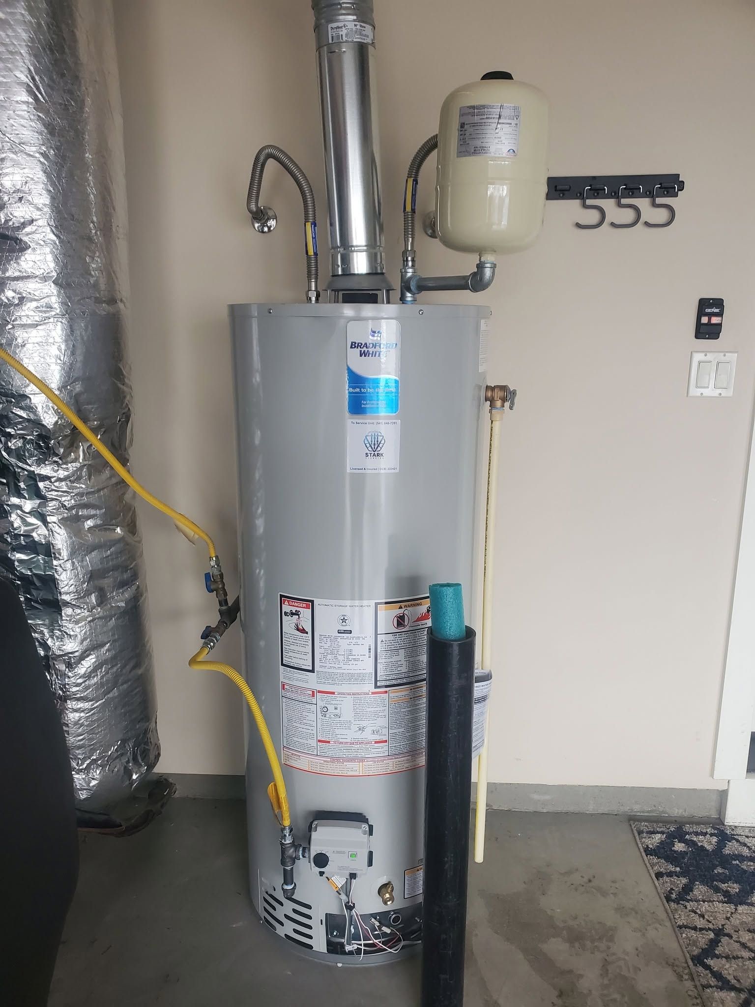Residential water heater with pipes and an expansion tank in a utility room, next to unit number 555.