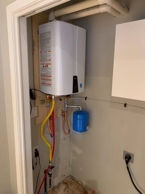 Wall-mounted water heater with pipes and blue expansion tank in a utility closet
