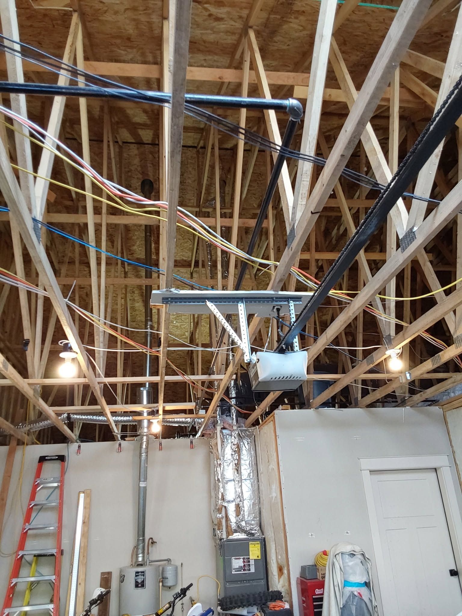 Construction site interior with exposed ceiling beams, ductwork, ladders, and hanging lights.