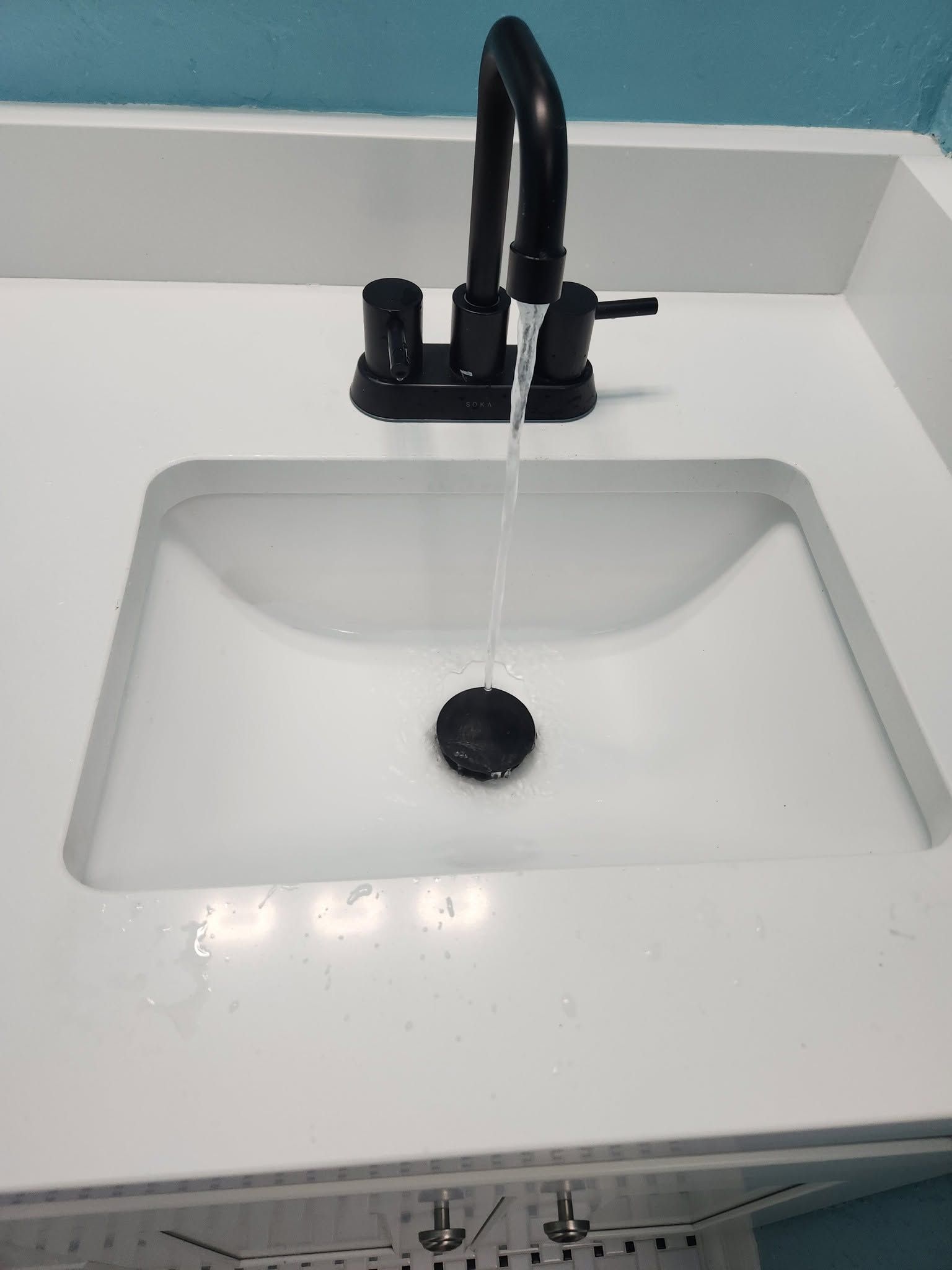 Black faucet running water into a white bathroom sink with a drain stopper.